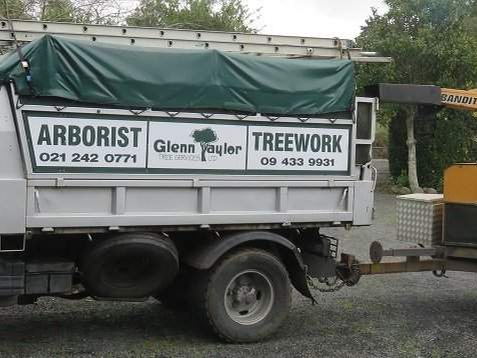 The blue Glenn Taylor Tree Services arborist truck towing a Bandit wood chipper